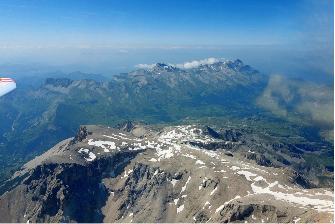 Das Bild zeigt eine spektakuläre Aussicht auf die französischen Westalpen aus einem Duodiskus-Segelflugzeug. Schneebedeckte Gipfel dominieren den Vordergrund, während sich grüne Täler und ferne Bergketten im Hintergrund erstrecken. Der Himmel ist strahlend blau mit nur wenigen Wolken – eine friedliche, majestätische Szene in großer Höhe.
Blick vom Pic de Bure nach Richtung Grenoble